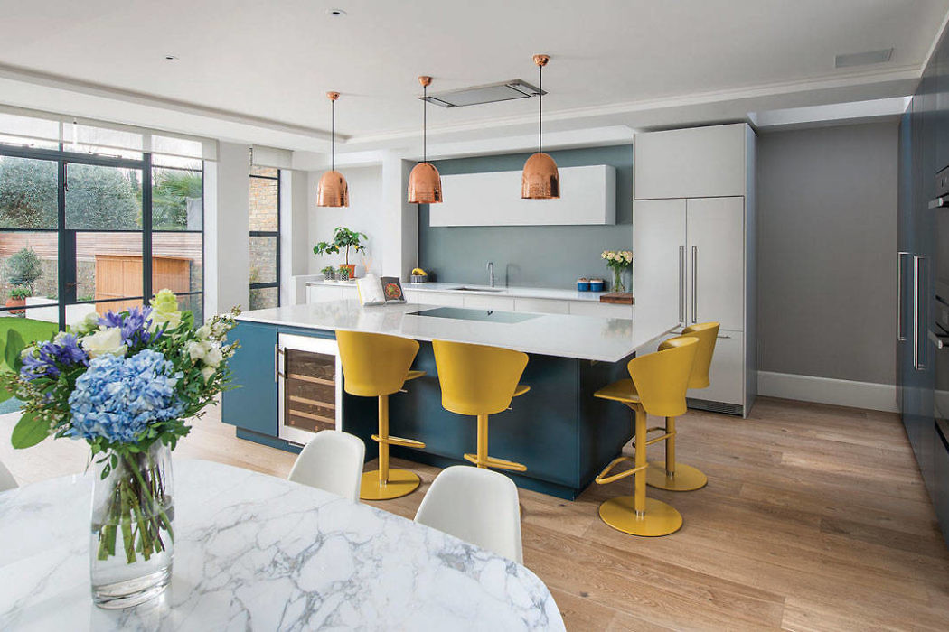 Modern kitchen with marble island, yellow stools, and copper pendants.