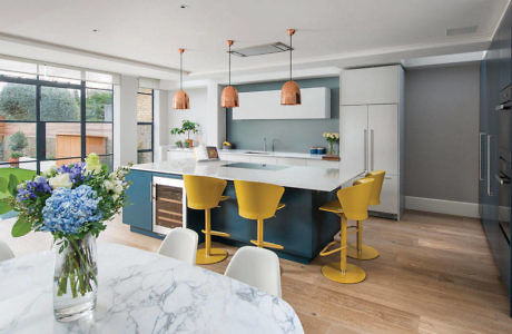 Modern kitchen with marble island, yellow stools, and copper pendants.