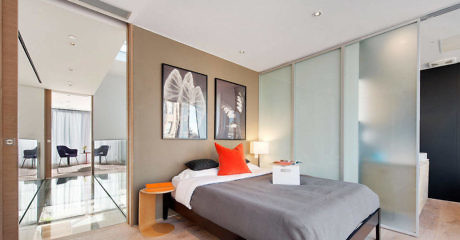 Modern bedroom with a grey bed, orange accents, and frosted glass partition.