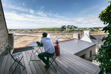 Two people on a seaside balcony with a view of the beach and houses.