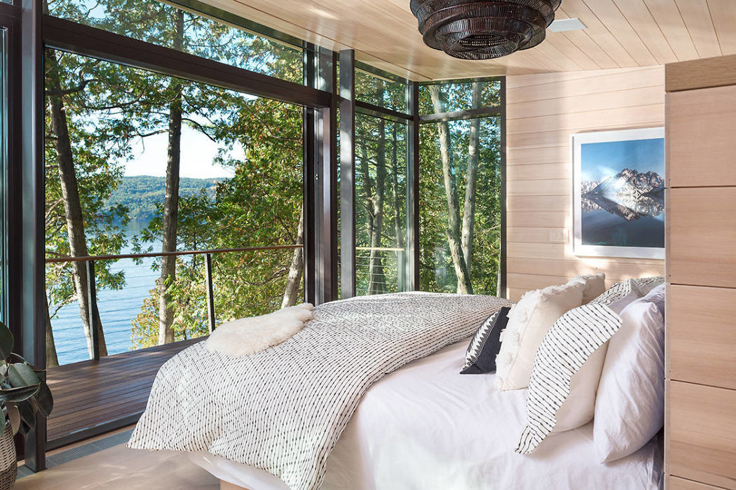 Modern bedroom with large windows overlooking a forest and lake.