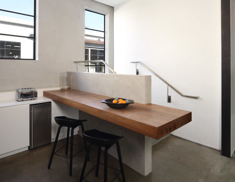Modern kitchen with a floating wooden table, black stools, and concrete elements.