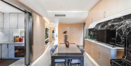 Modern kitchen interior with wood finishes, black marble accent, and motion-blurred person