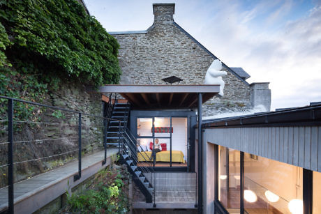 Stone house with modern glass extension and exterior staircase at twilight.