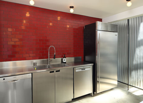 Stainless steel kitchen with red brick wall and corrugated metal.
