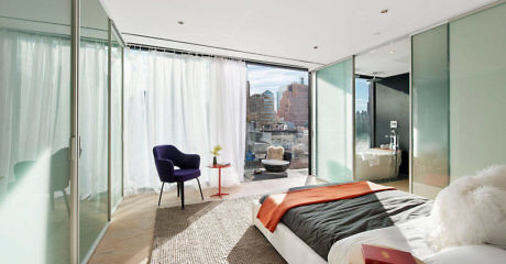 Sleek bedroom with glass walls and city view.