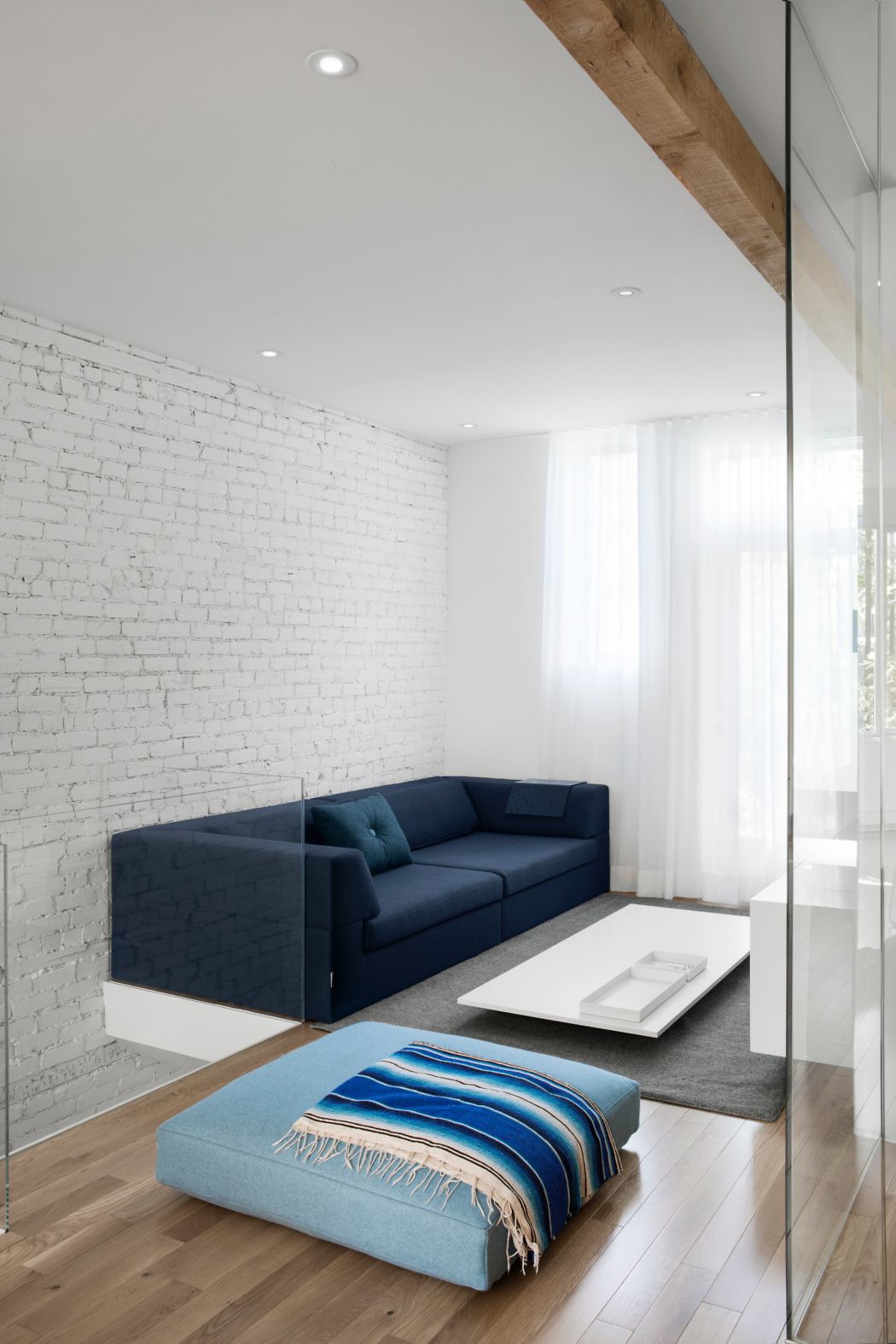 Minimalist living room with a blue sofa, white brick wall, and wooden beams