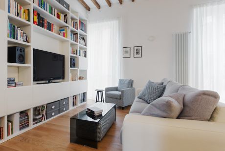 Modern living room with white bookshelf, sofa, TV, and wooden floor.