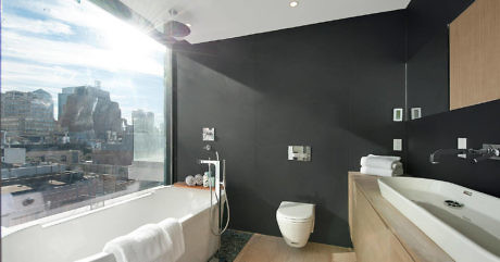 Modern bathroom with city view, featuring a bathtub, toilet, and sink.