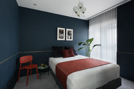 Modern bedroom with dark blue walls, red accents, and a plant.