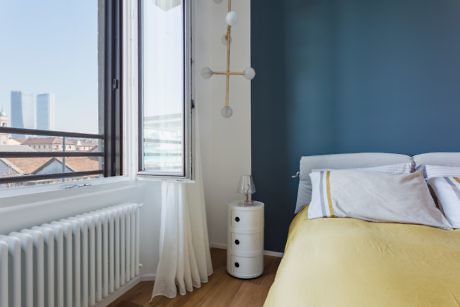 Modern bedroom with a blue wall, white curtains, and a yellow bedspread.