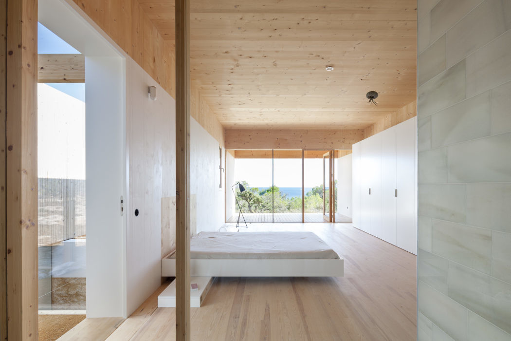 Minimalist bedroom with wooden floors and walls, large windows, and a simple bed