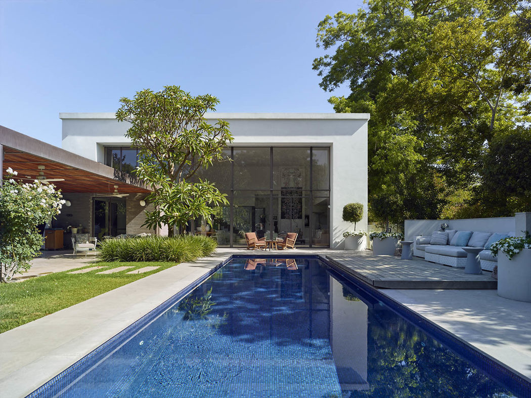 Modern house with pool, patio furniture, and trees under a clear sky.