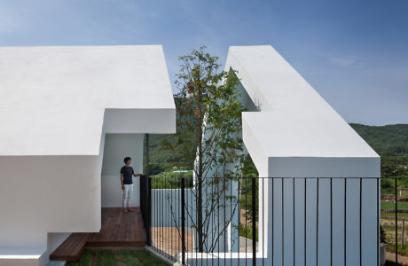 Geometric white building with person at entrance, blue fence, and green backdrop.