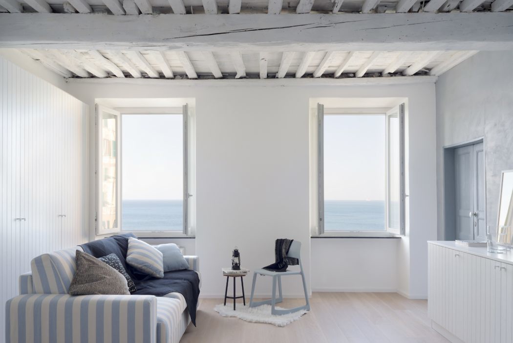 Coastal-style interior with sea view, striped sofa, and exposed ceiling beams