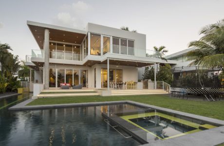 Modern two-story house with large windows, pool, and patio at dusk.