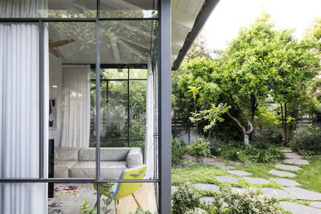 Contemporary living room viewed through large windows with lush garden outside.