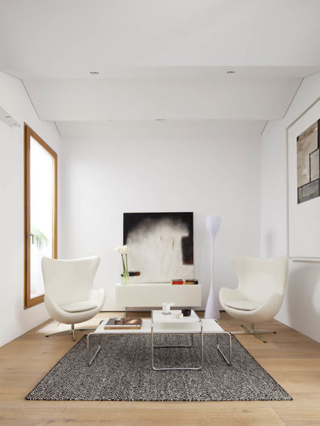 Minimalist living room with white chairs and a sleek TV setup.