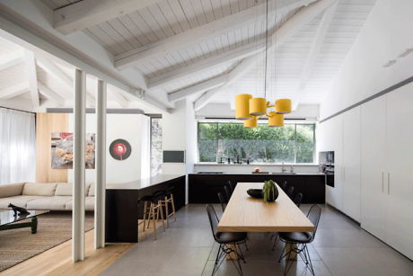 Modern kitchen with white walls, black countertops, wooden table, and yellow pendant lights