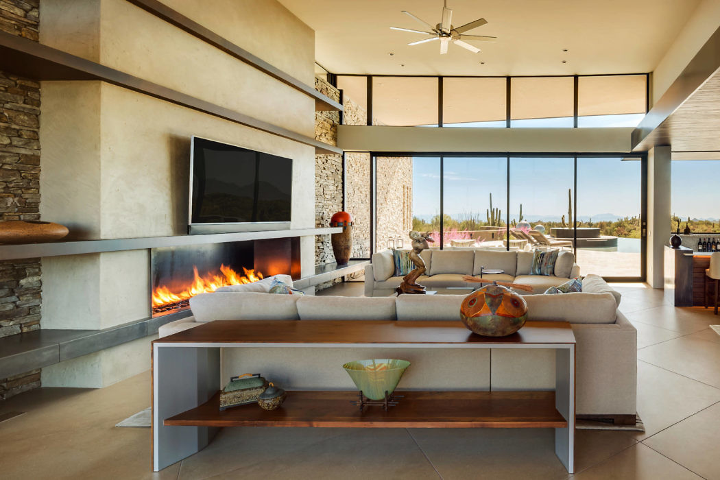 Modern living room with fireplace, sofa, and large windows overlooking desert scenery.