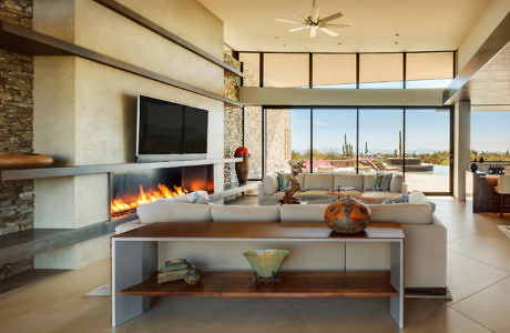 Modern living room with fireplace, sofa, and large windows overlooking desert scenery.