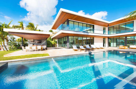 Modern house with large windows, poolside loungers, and a palm garden.