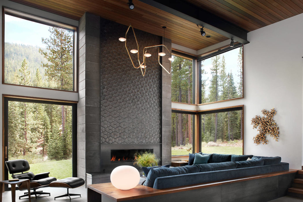 Modern living room with large windows, a fireplace, and forest view.