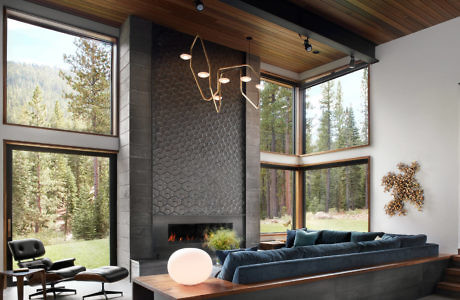 Modern living room with large windows, a fireplace, and forest view.