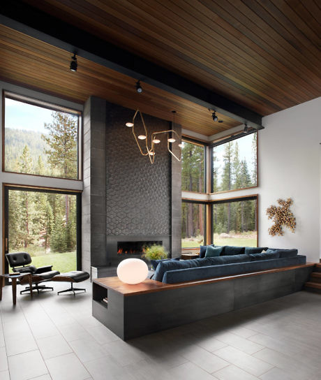 Modern living room with large windows, a fireplace, and forest view.