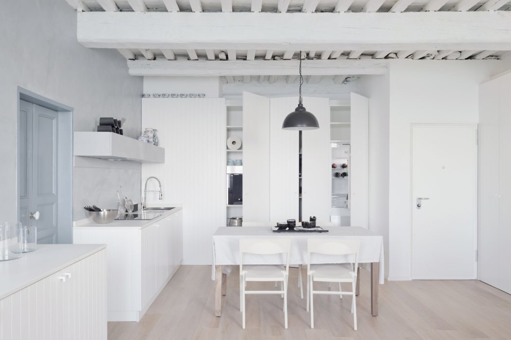 Modern white kitchen with dining area and exposed ceiling beams.