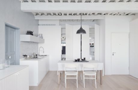 Modern white kitchen with dining area and exposed ceiling beams.