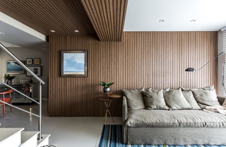 Modern living room with wooden slatted walls, grey sofa, and a staircase.