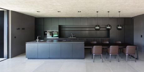 Modern kitchen with dark cabinetry, island, pendant lights, and dining chairs.