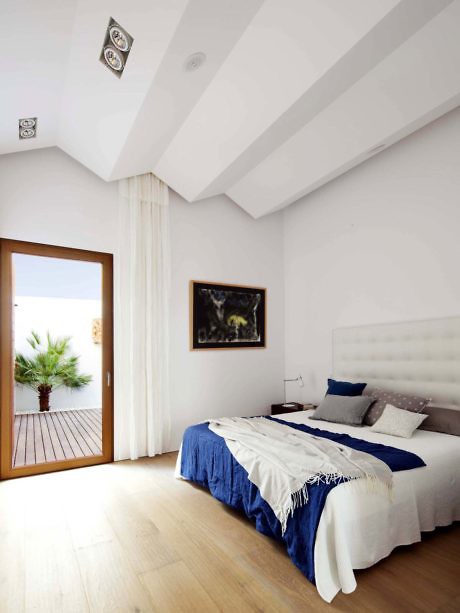 Bright, modern bedroom with white walls, wooden floor, and blue bedding.