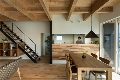 Modern kitchen with wooden design elements, person at counter, staircase on the left.