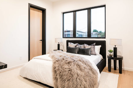Modern bedroom with large windows, white bedding, and gray accents.