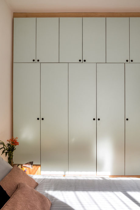 Minimalist bedroom with a large, modern wardrobe and sunlight casting shadows.