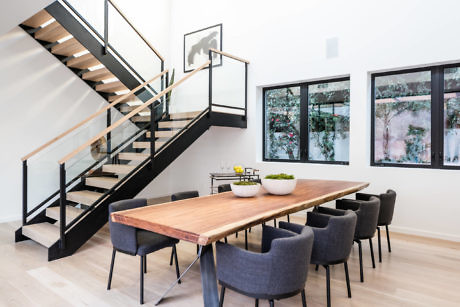 Modern dining room with wooden table, chairs, and floating staircase.