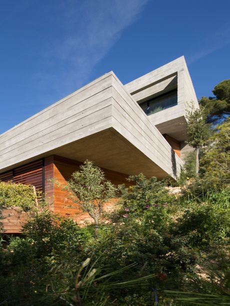 Modern angular concrete house with wooden elements surrounded by trees.