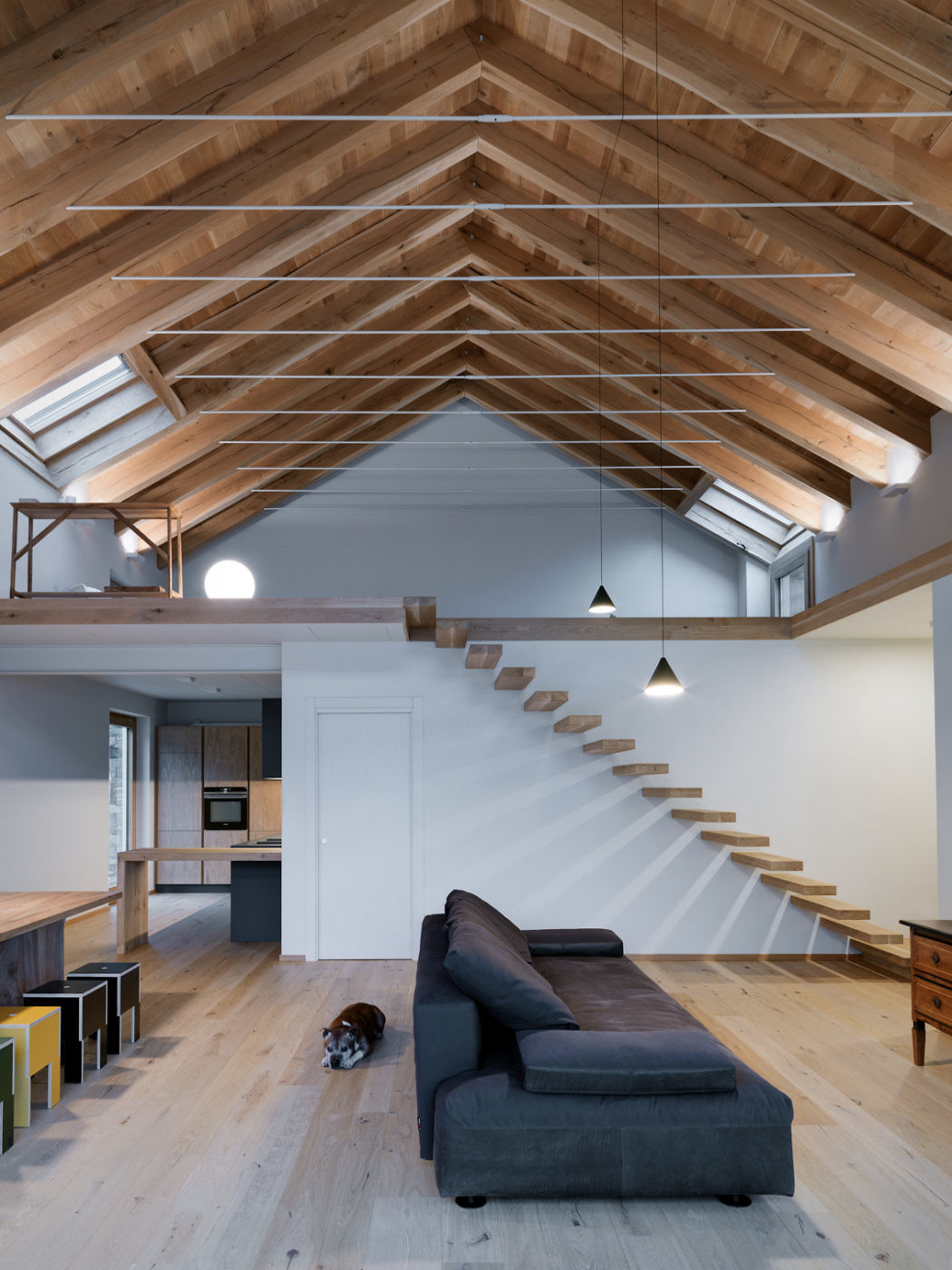 Spacious loft with exposed wooden beams, floating staircase, and a cozy seating area