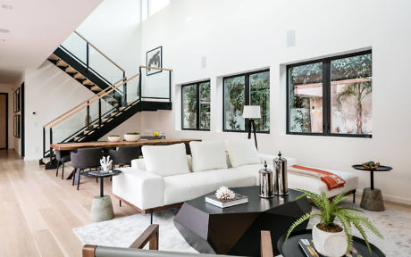 Modern living room with white sofa, black stairs, and large windows.