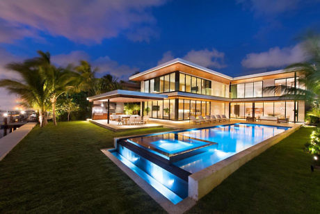 Luxurious seaside villa with pool and large glass windows at dusk.