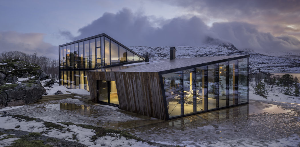 Contemporary glass house with wooden accents in a snowy landscape at dusk.