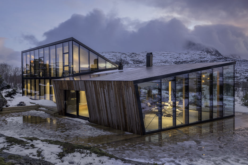 Contemporary glass house with wooden accents in a snowy landscape at dusk.