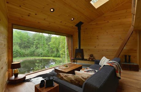 Wood-paneled cabin interior with large window overlooking a pond.