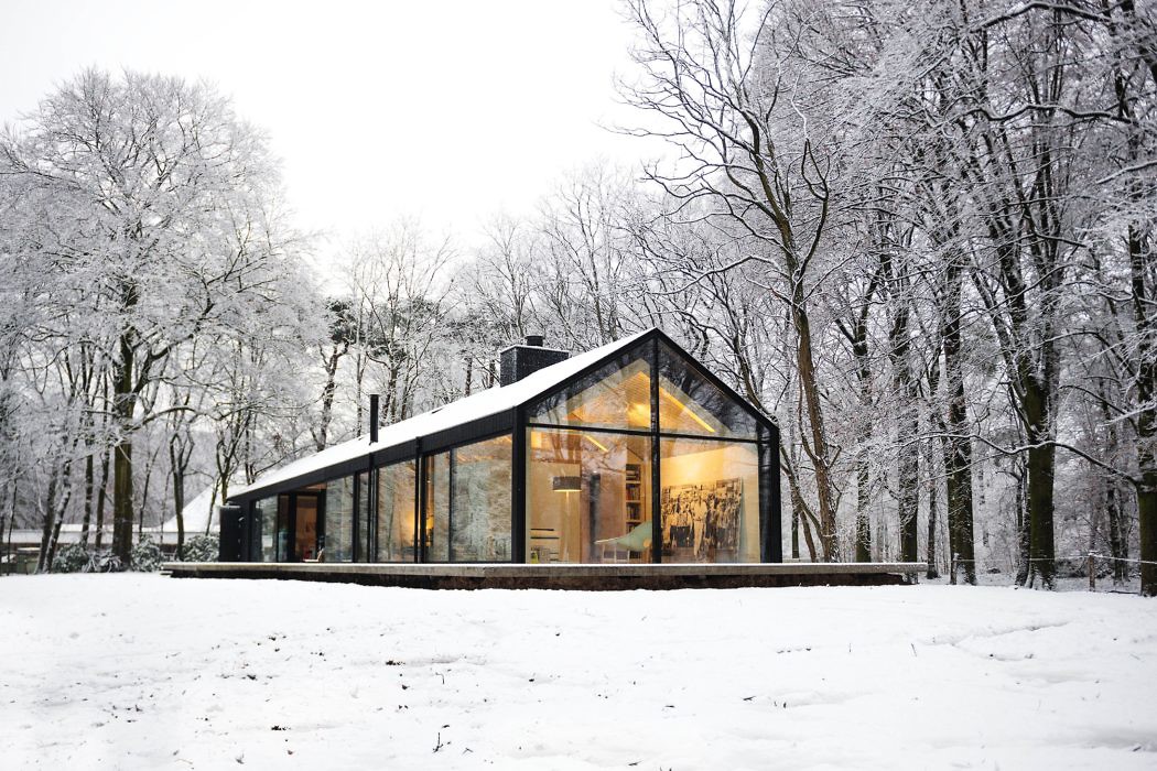 Contemporary glass house amidst snowy forest.