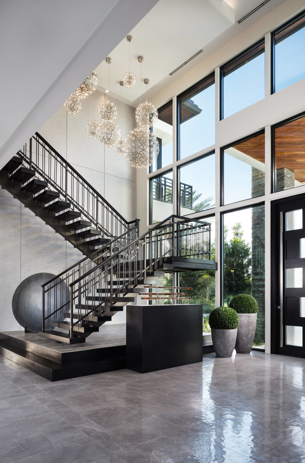 Elegant foyer with a modern staircase, large windows, and chandeliers.
