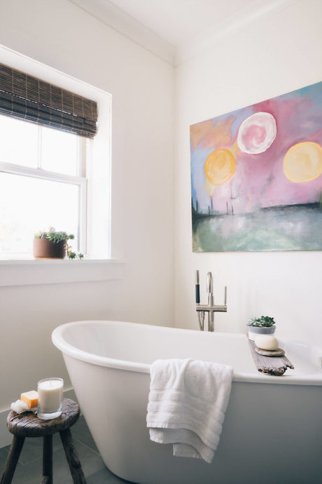 Bright bathroom with freestanding tub and colorful artwork.
