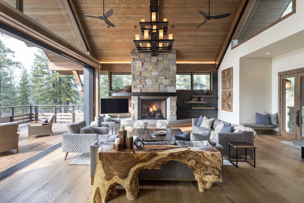 Luxurious living room with a stone fireplace, wooden ceiling, and expansive windows.