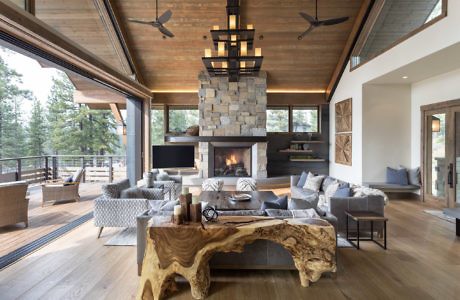 Luxurious living room with a stone fireplace, wooden ceiling, and expansive windows.